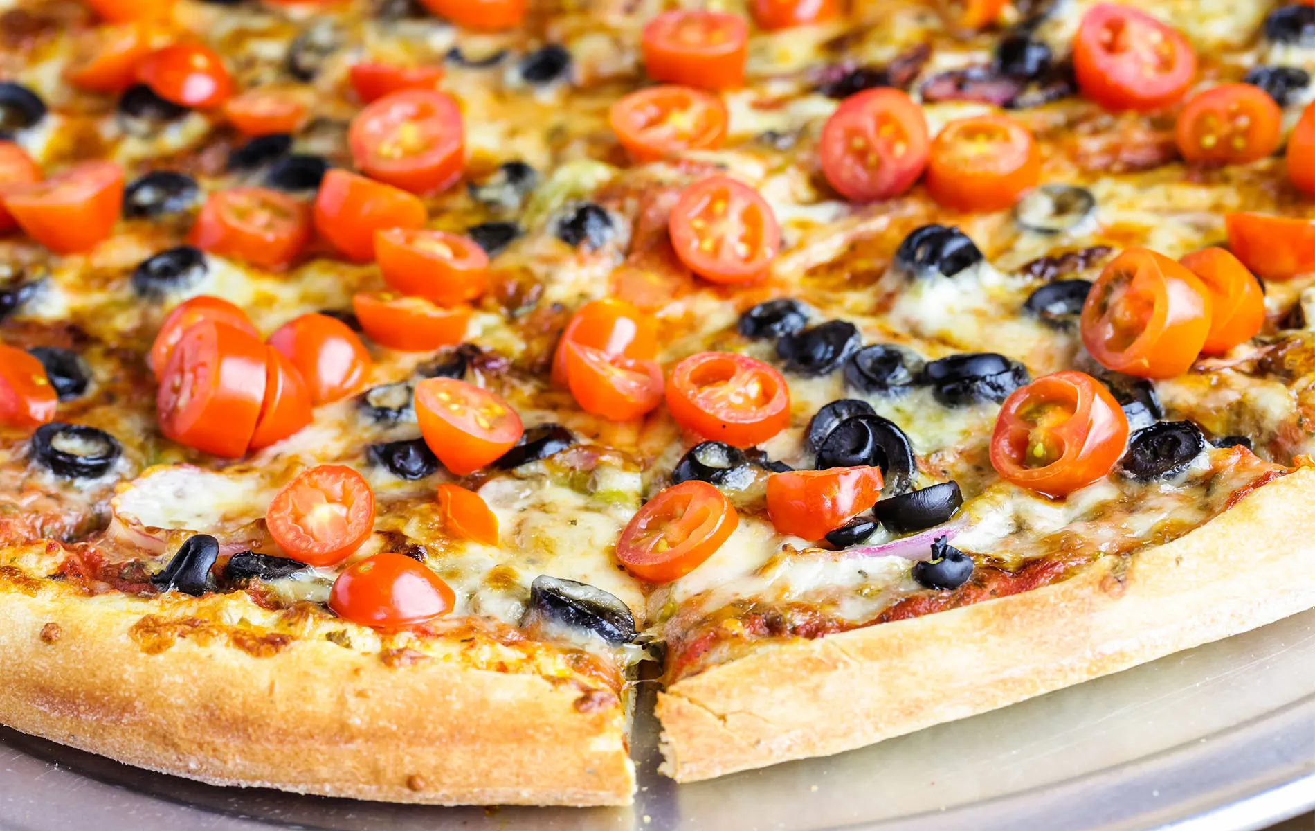 A thin crust pizza topped with cherry tomatoes and black olives