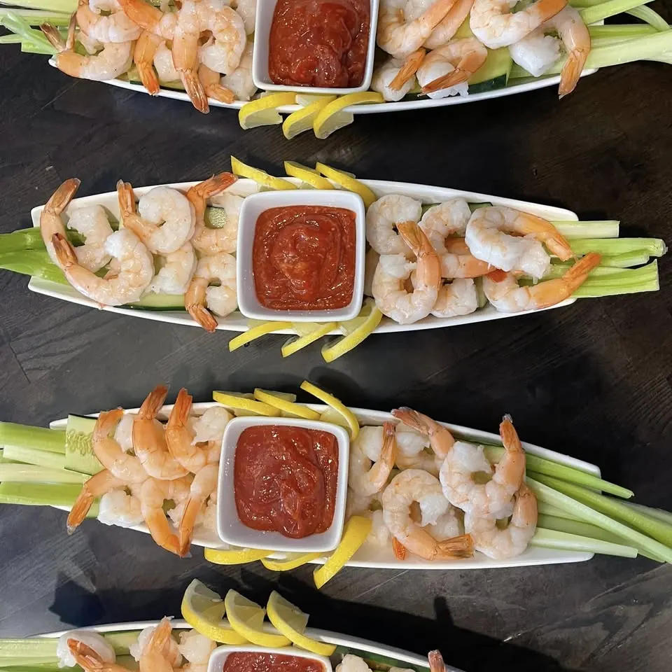 Four platters of shrimp cocktail with celery, lemon and cocktail sauce